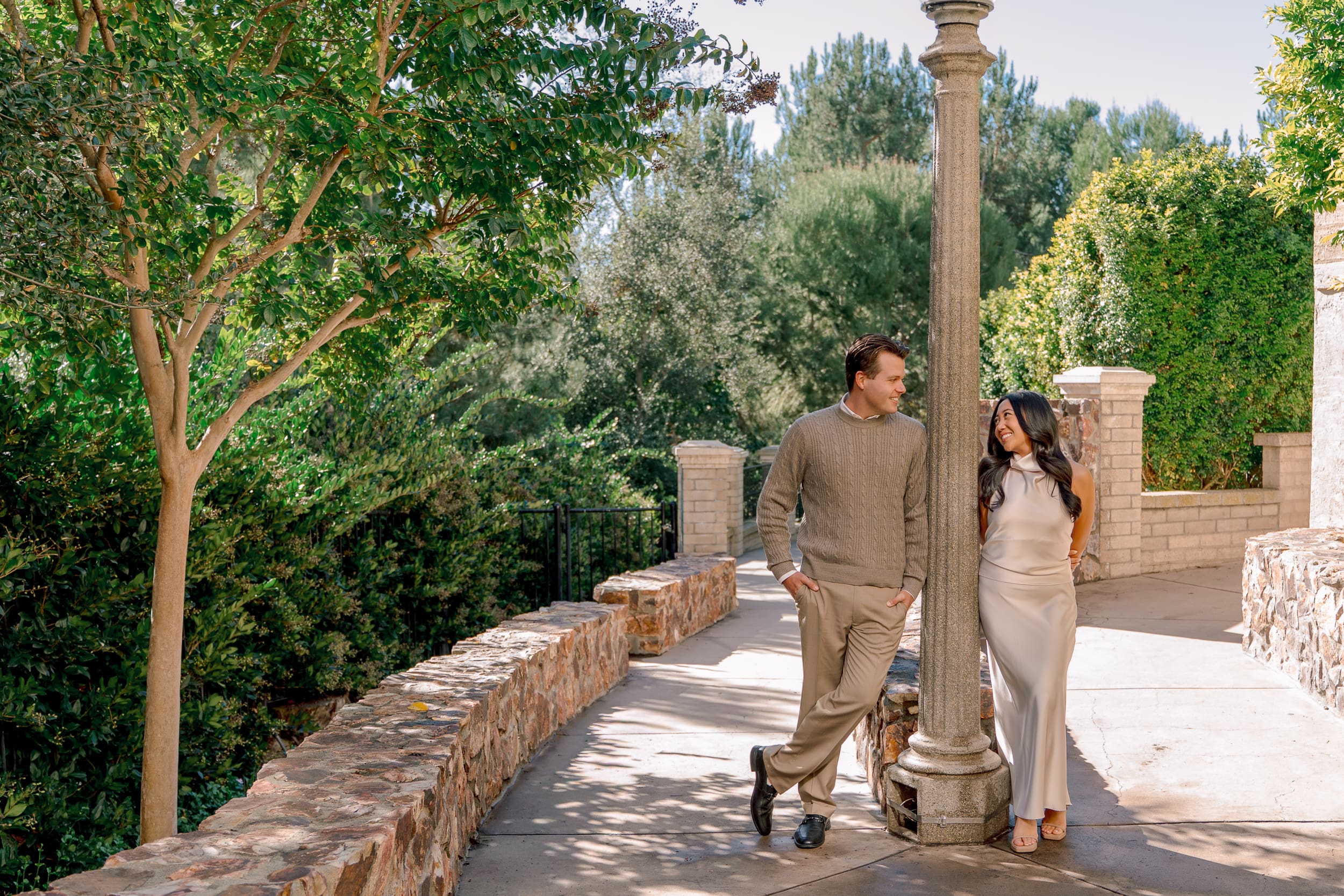Engaged couple leaning against a lamppost and smiling at each other during their Balboa Park engagement photoshoot with San Diego photographer Ro Banner.