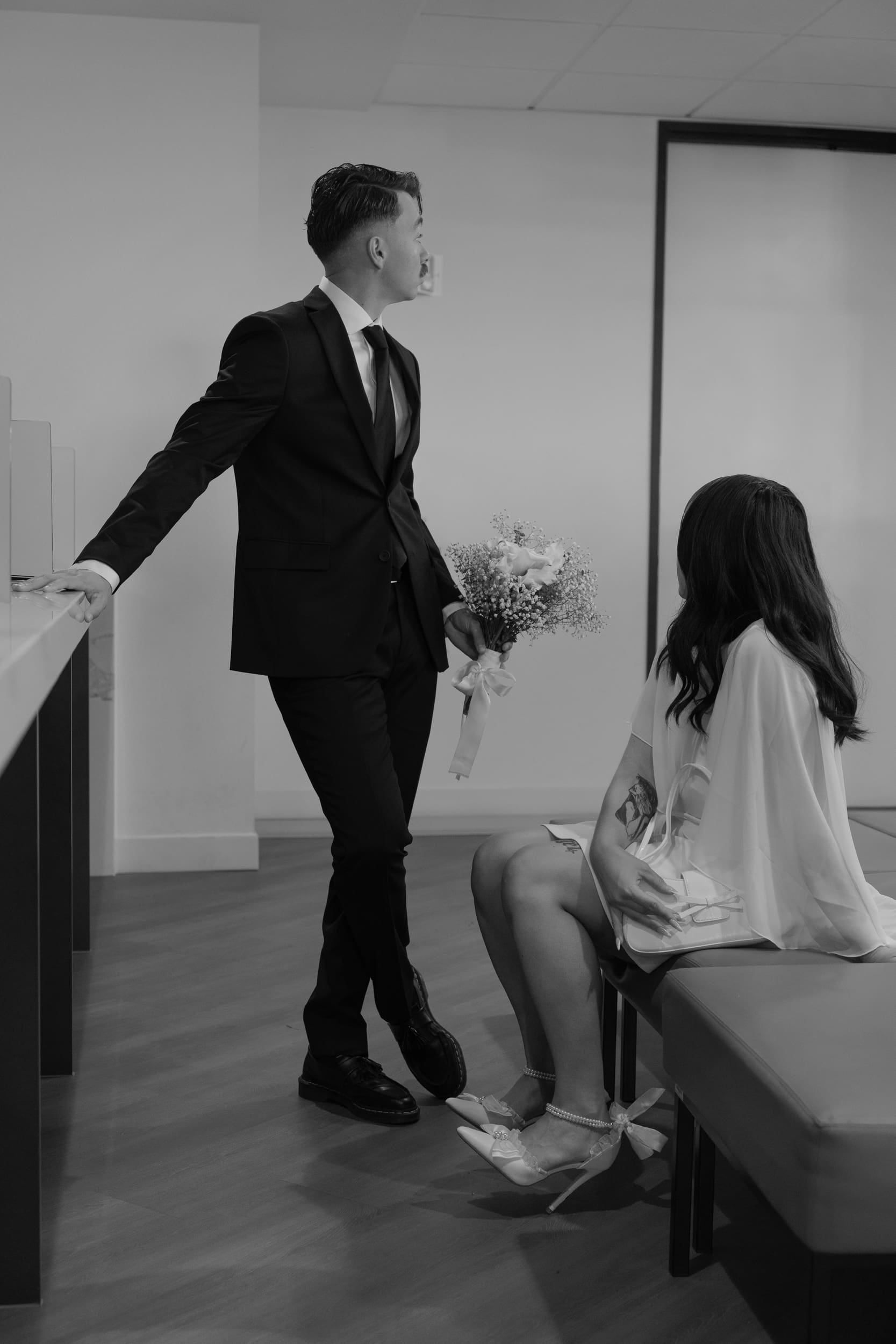 Bride and groom sitting closely together on a courthouse bench during their San Diego elopement, captured in a quiet candid black-and-white documentary style.