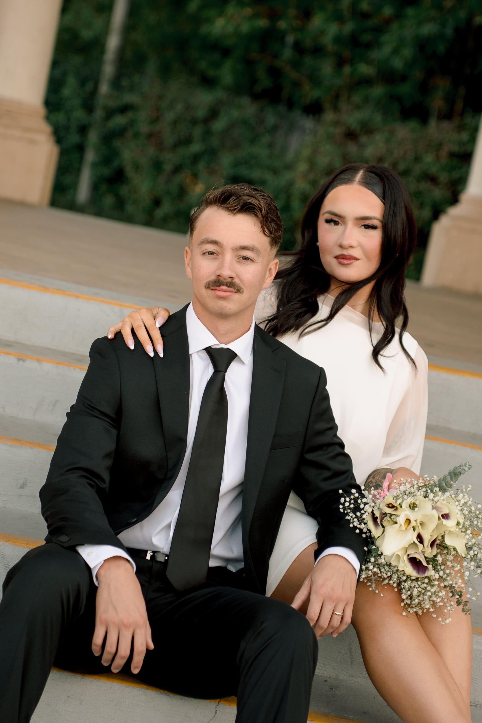 Bride and groom sitting together on the steps at Balboa Park during their San Diego courthouse wedding, captured in a soft true-to-color editorial portrait style