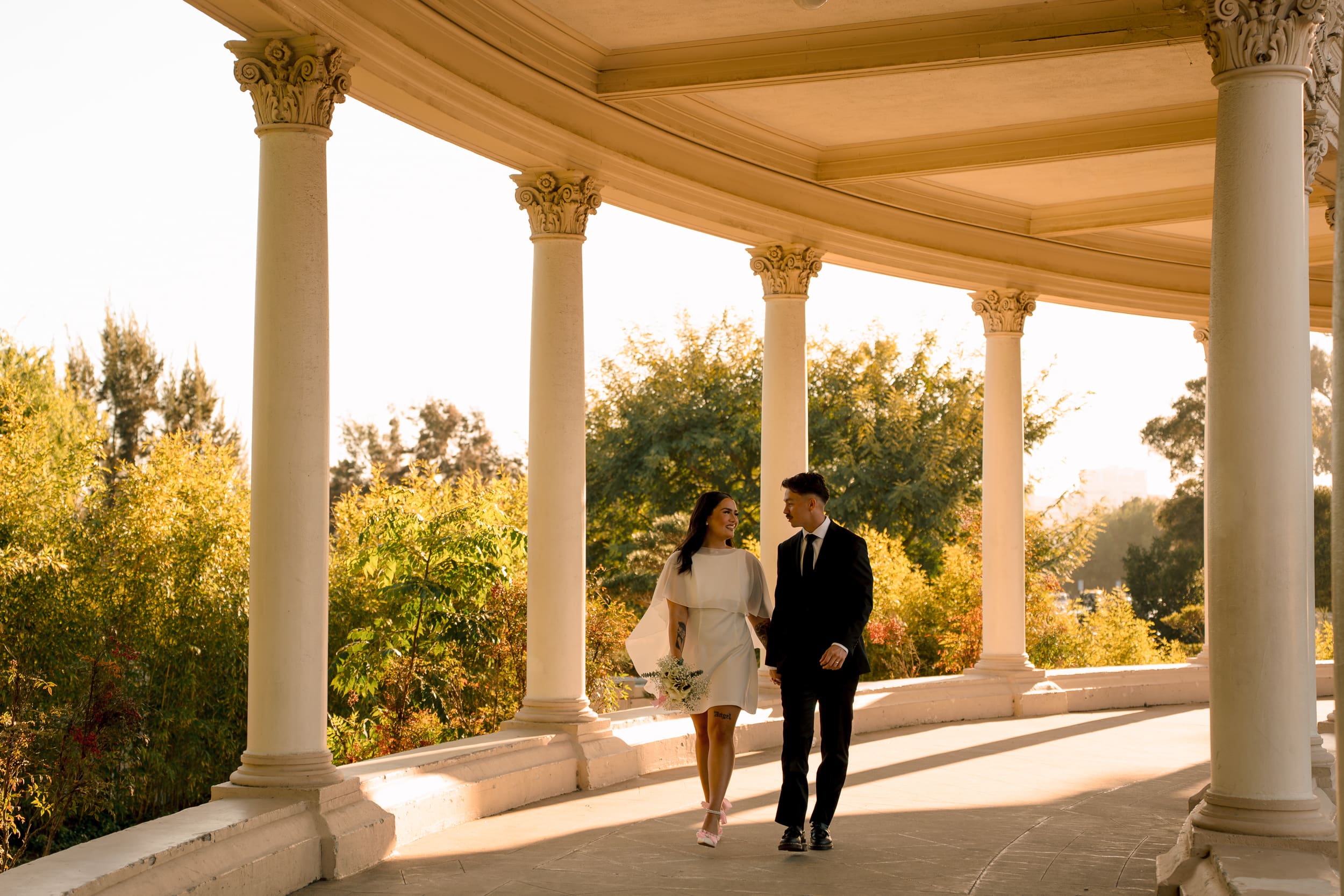 Bride and groom walking hand in hand under the arches at Balboa Park during their San Diego courthouse elopement, photographed in warm golden-hour documentary style