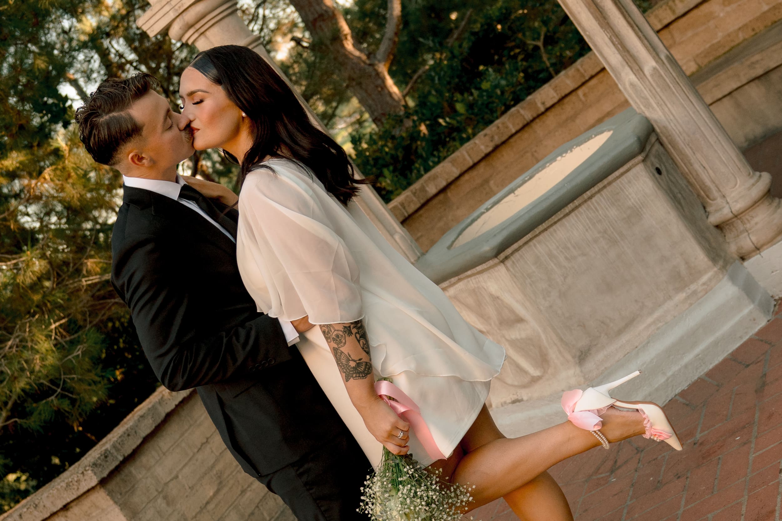 Bride and groom walking hand in hand under the arches at Balboa Park during their San Diego courthouse elopement, photographed in warm golden-hour documentary style