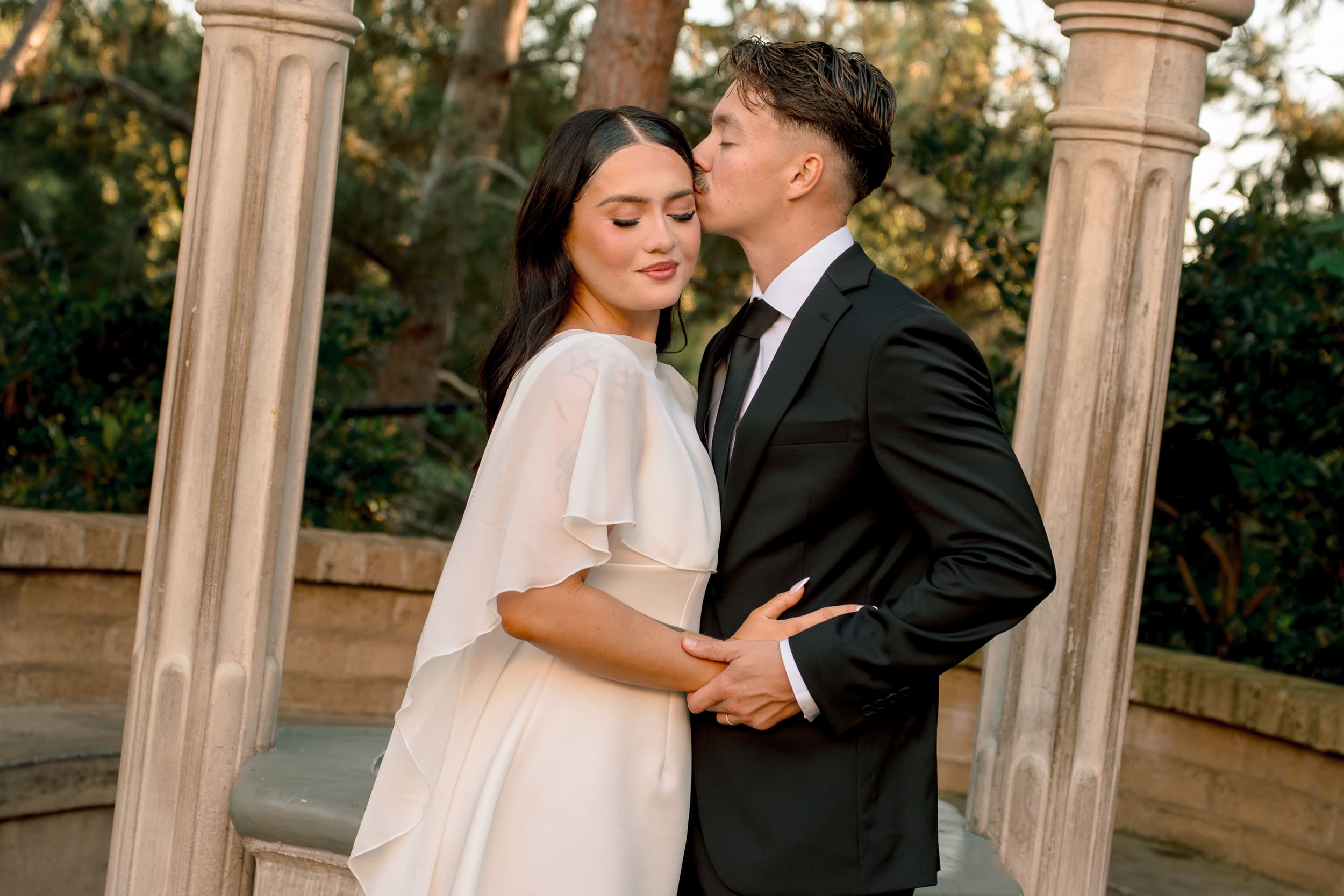 Bride and groom sharing a kiss by the stone fountain at Balboa Park during their San Diego courthouse wedding portraits, captured in a romantic cinematic style.