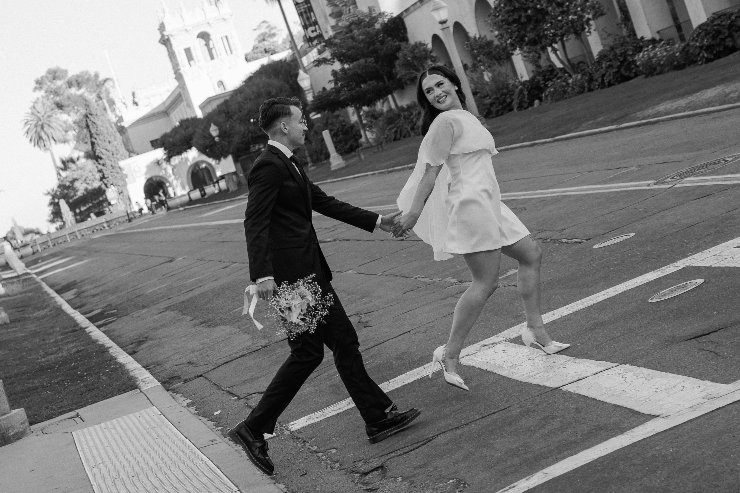 Bride and groom walking hand in hand under the arches at Balboa Park during their San Diego courthouse elopement, photographed in warm golden-hour documentary style