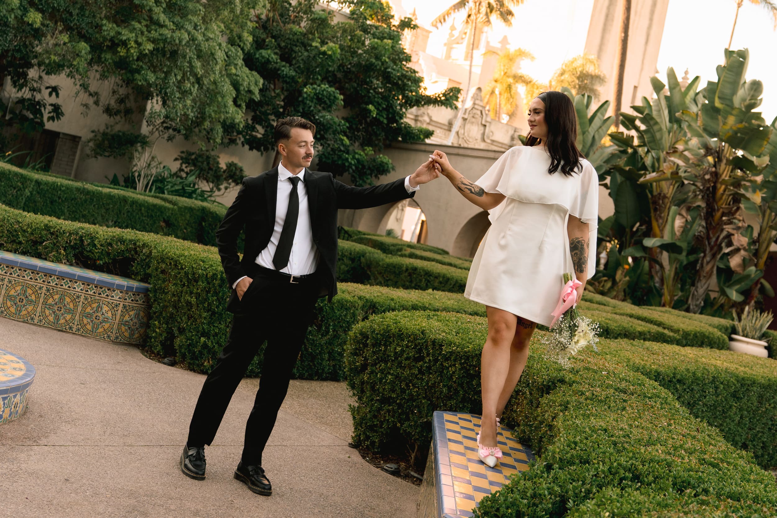 Groom helping his bride step down in the garden maze at Balboa Park during their San Diego courthouse elopement, captured in a soft true-to-color documentary editorial style.