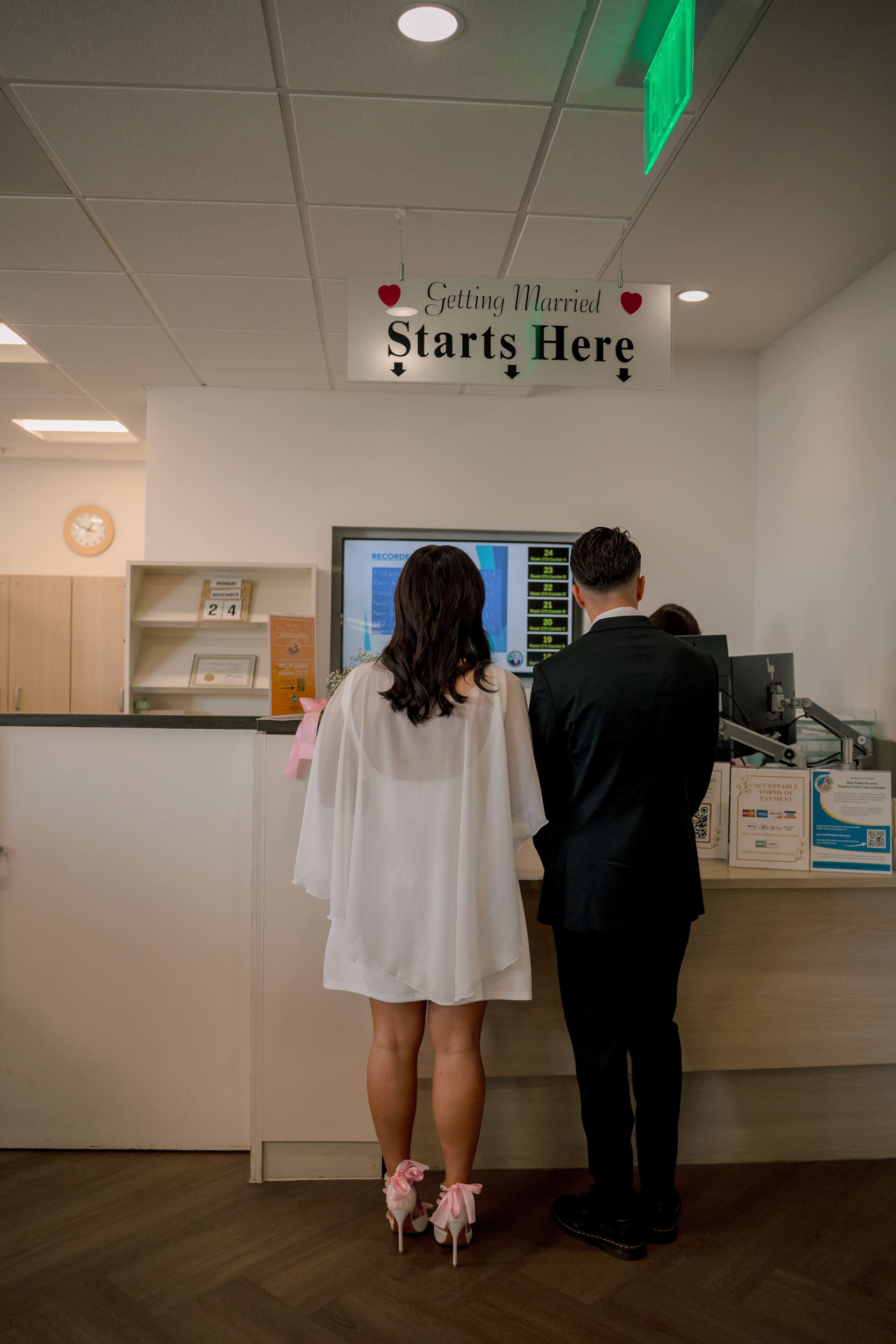 Bride and groom checking in at the San Diego courthouse under the ‘Getting Married Starts Here’ sign during their elopement, photographed in a candid documentary style.